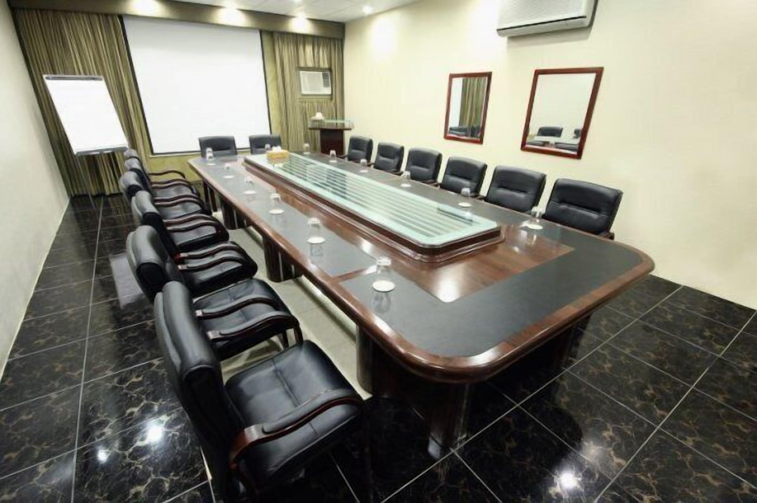A conference room with a long table, black leather chairs, a projector screen, and a podium.