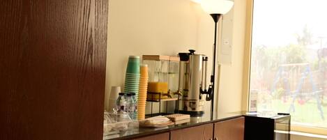 A kitchen counter with a coffee maker, stacked cups, and a window with a view of a garden.