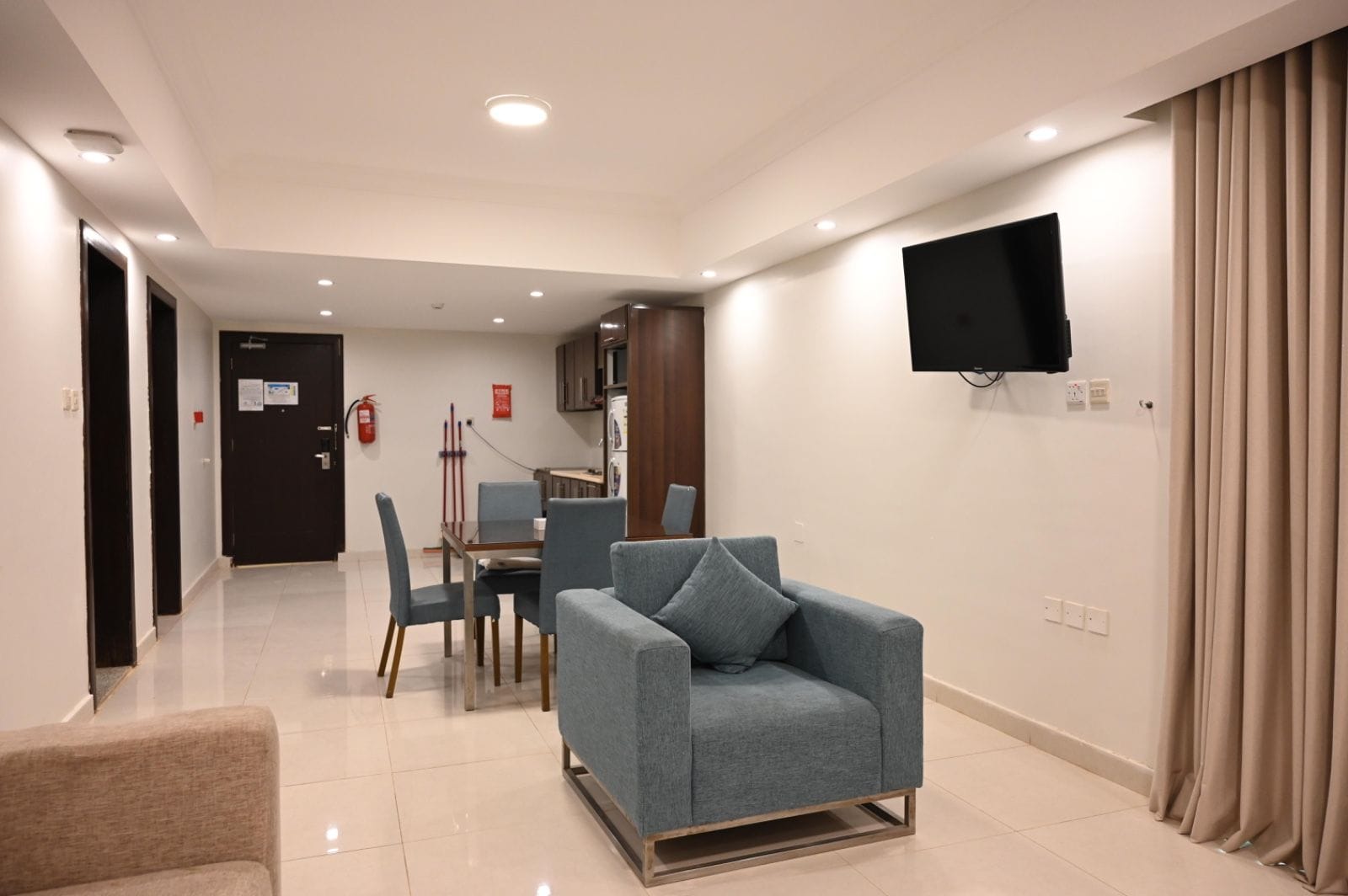 A hotel room with a seating area, a flat-screen TV mounted on the wall, and a door leading to another room.