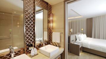 Habitación de hotel con un espejo grande, una mesita de noche, una cama y un baño con lavamanos y espejo.