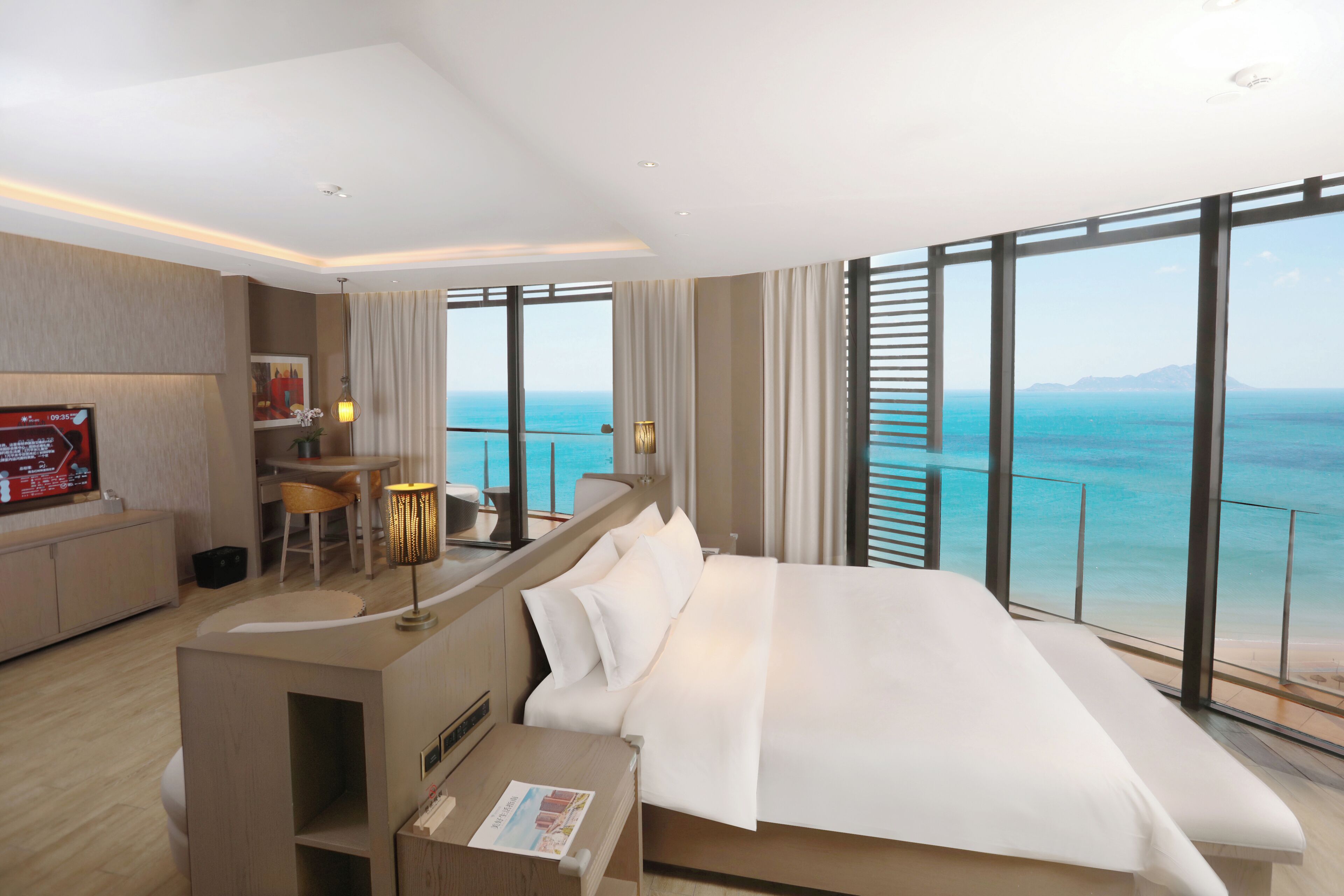 A modern hotel room with a large bed, a desk, and a view of the ocean.