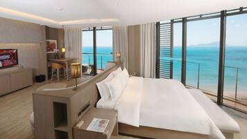 A modern hotel room with a large bed, a desk, and a view of the ocean.