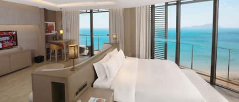 A modern hotel room with a large bed, a desk, and a view of the ocean.