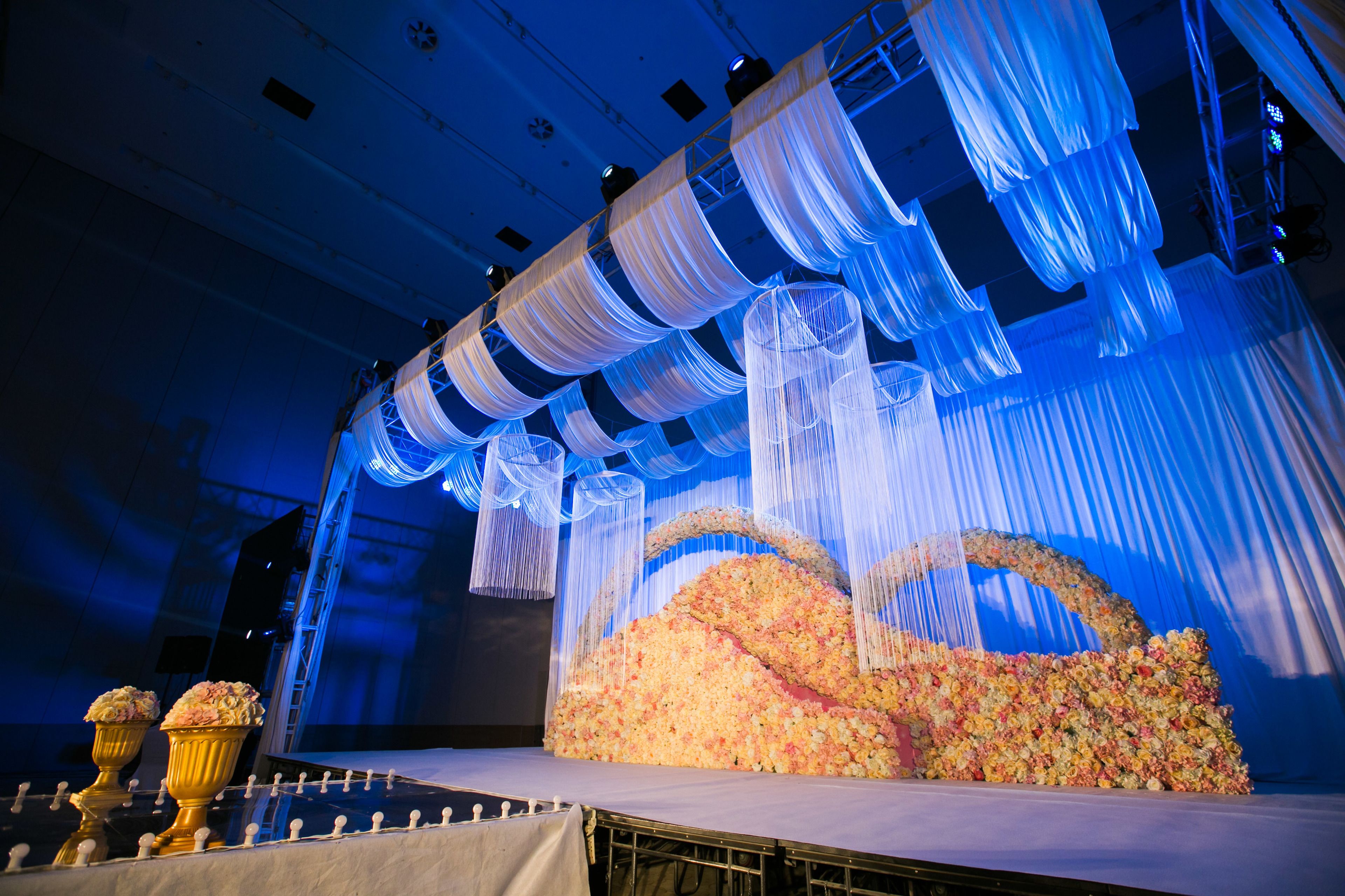 A stage with a floral arrangement, draped fabric, and golden vases.