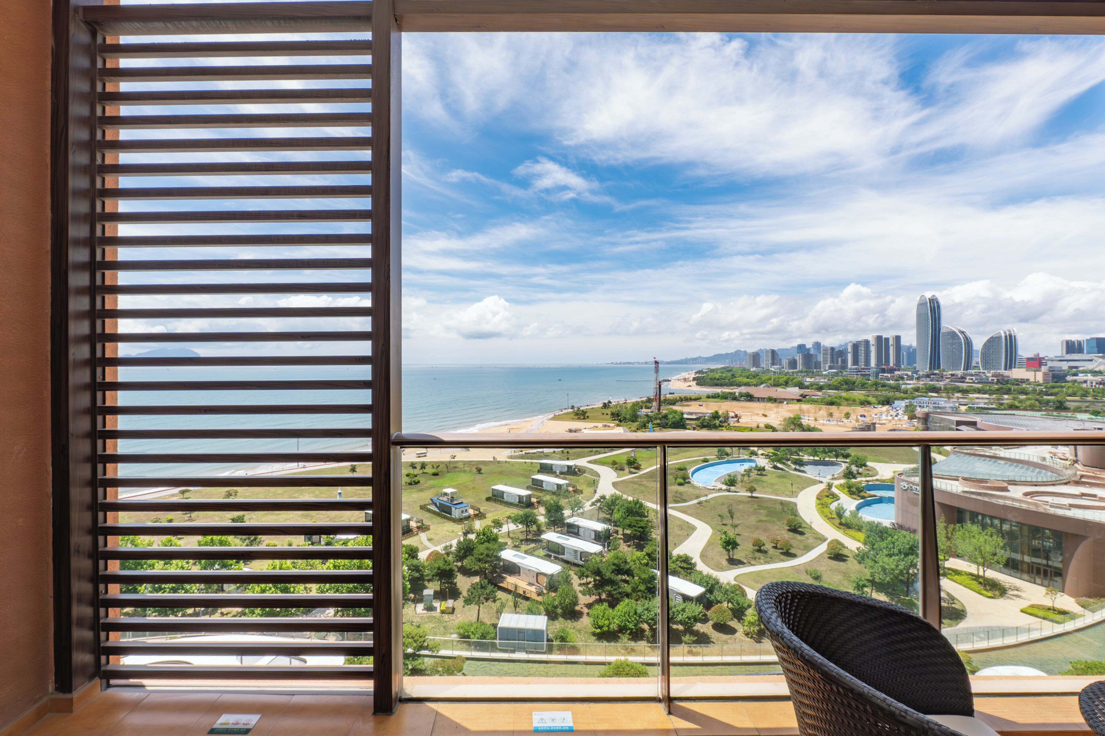 A balcony with a view of a beach, city skyline, and a swimming pool complex.