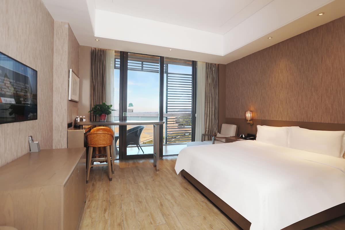 Ett modernt hotellrum med en stor säng, ett skrivbord med en stol, en TV och en balkong med utsikt.