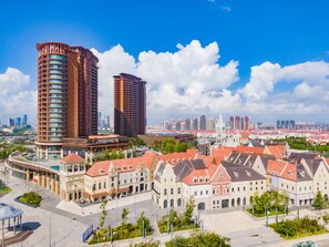 A modern hotel with a curved facade, a central courtyard, and a view of the city skyline. - Mangrove Tree Resort World Qingdao (Qingdao)