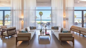 A spacious lobby with a view of the beach, featuring a sofa set, a coffee table, and a floor lamp.