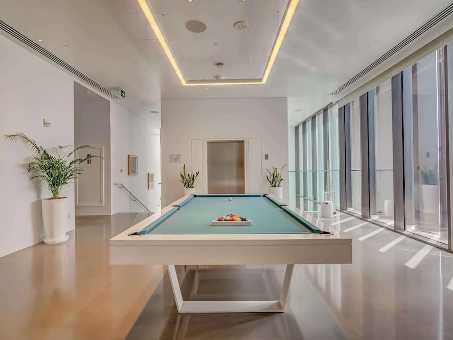 Ein moderner Indoor-Biliardtisch mit grüner Spielvliesplatte, umgeben von weißen Wänden und Topfpflanzen.