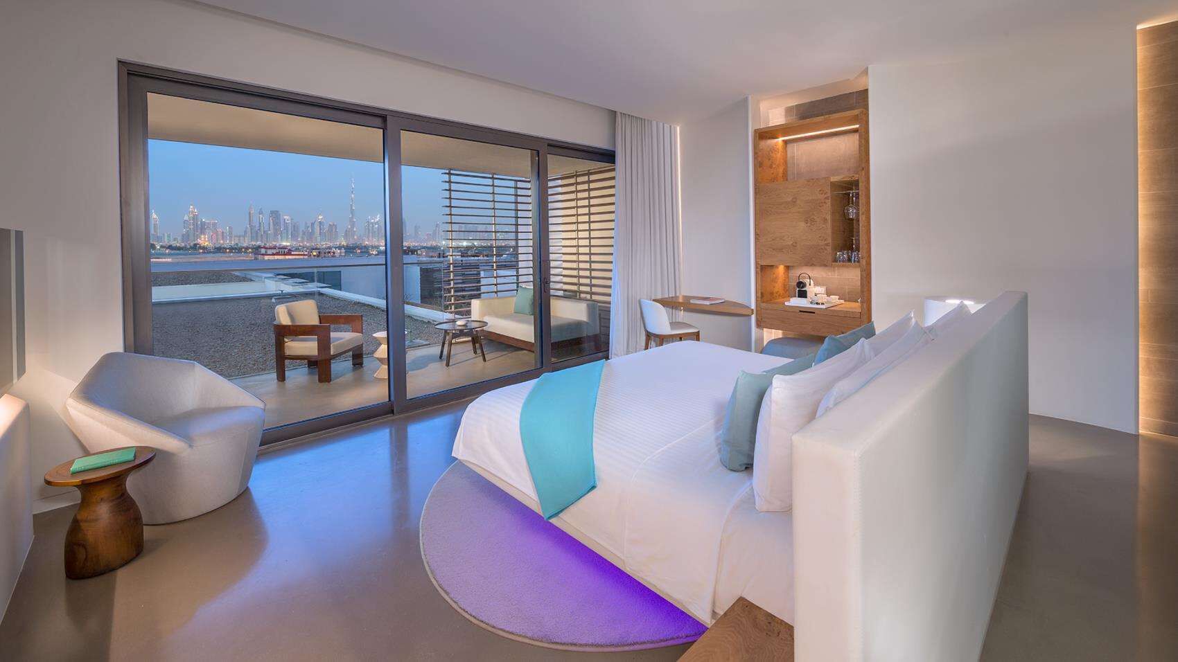 Une chambre d’hôtel moderne dotée d’un grand lit, d’un coin salon avec vue sur le paysage urbain et d’une petite kitchenette.