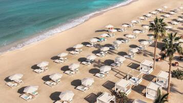 An aerial view of a beach with rows of sun loungers and umbrellas, arranged in a linear pattern along the shoreline.