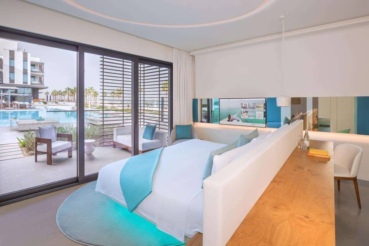 Een moderne hotelkamer met een groot bed, uitzicht op een zwembad en een balkon met buitenmeubilair.