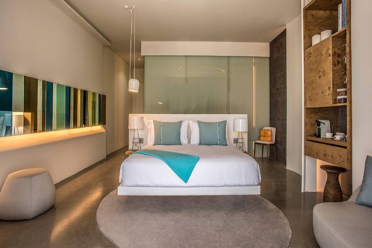 A modern hotel room with a large bed, bedside tables, a seating area, and a large window.