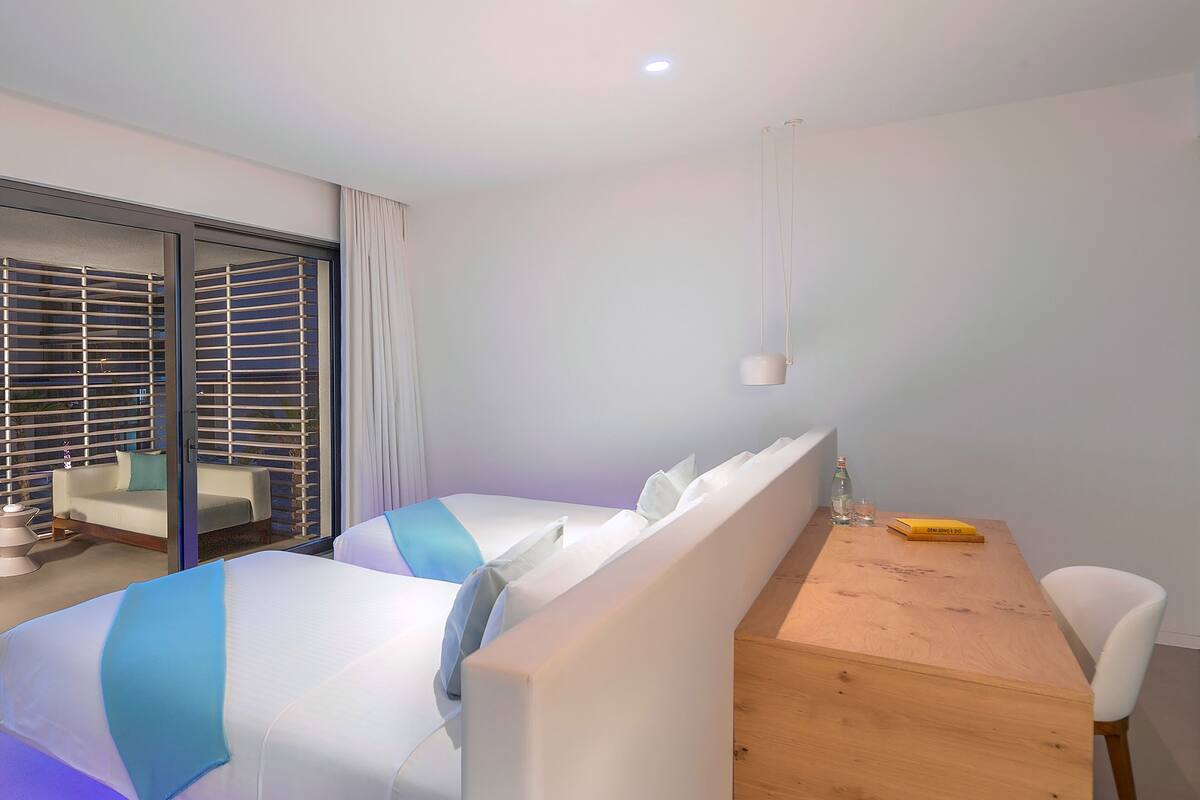 A modern hotel room with a large bed, a wooden desk, and a white chair.