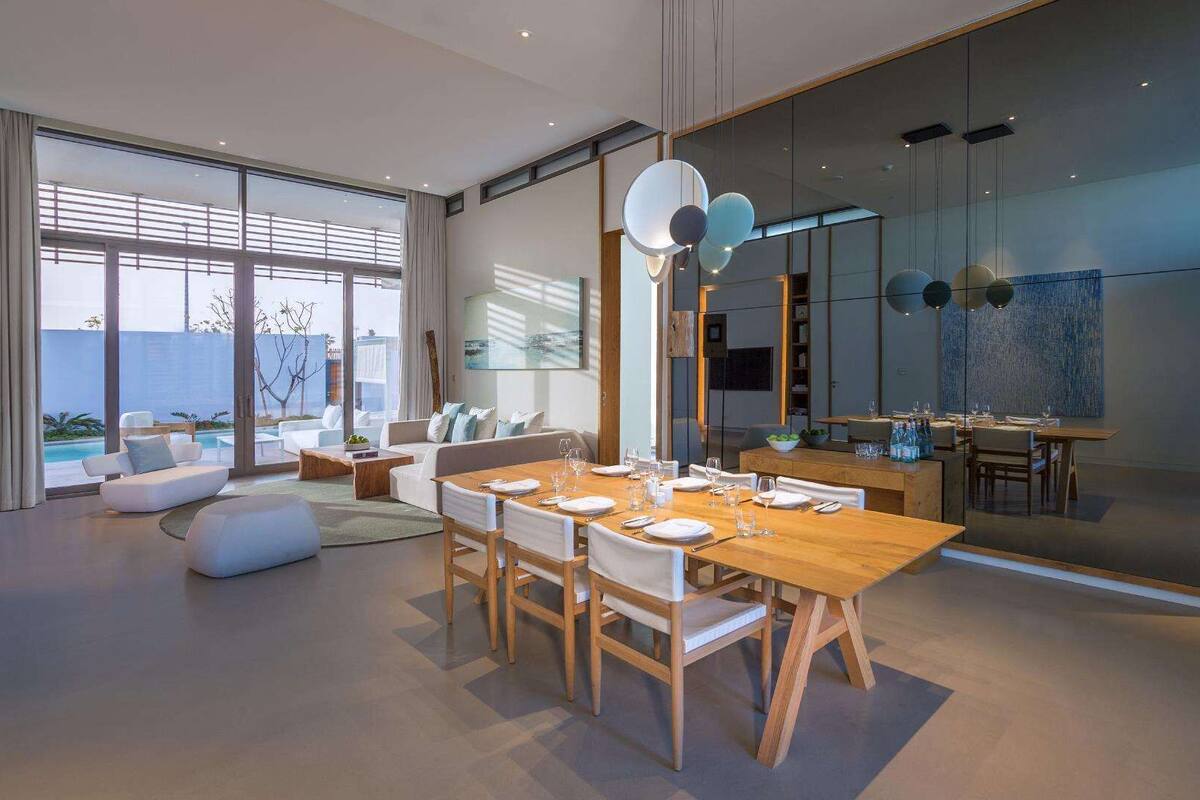 A modern dining area with a wooden table set for six, surrounded by white chairs.