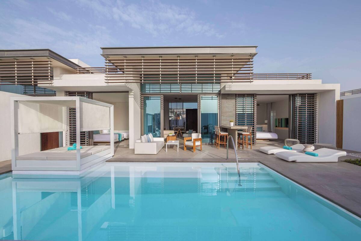 A modern poolside area with a clear pool, outdoor seating, and a contemporary building with large windows.
