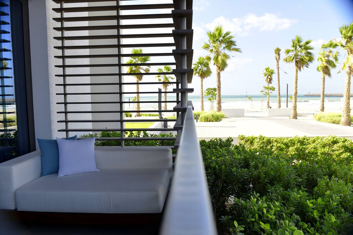 A modern outdoor seating area with a view of the beach and palm trees.