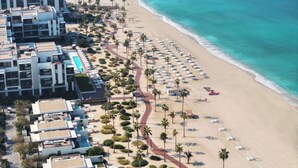 An aerial view of a coastal hotel with a beach, palm trees, and a rocky breakwater.