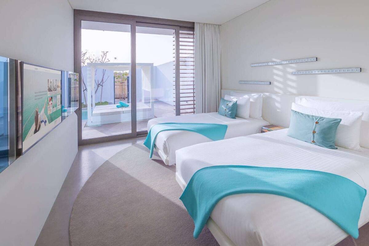 Een hotelkamer met twee bedden, een groot raam en uitzicht op een buitenruimte.