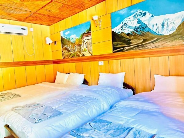 Une chambre d’hôtel avec deux lits, des lambris en bois, un tableau représentant une montagne et un appareil de climatisation.