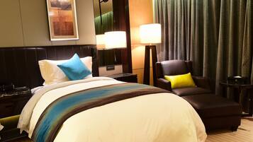 A hotel room with a large bed, a chair, a desk, and a lamp.