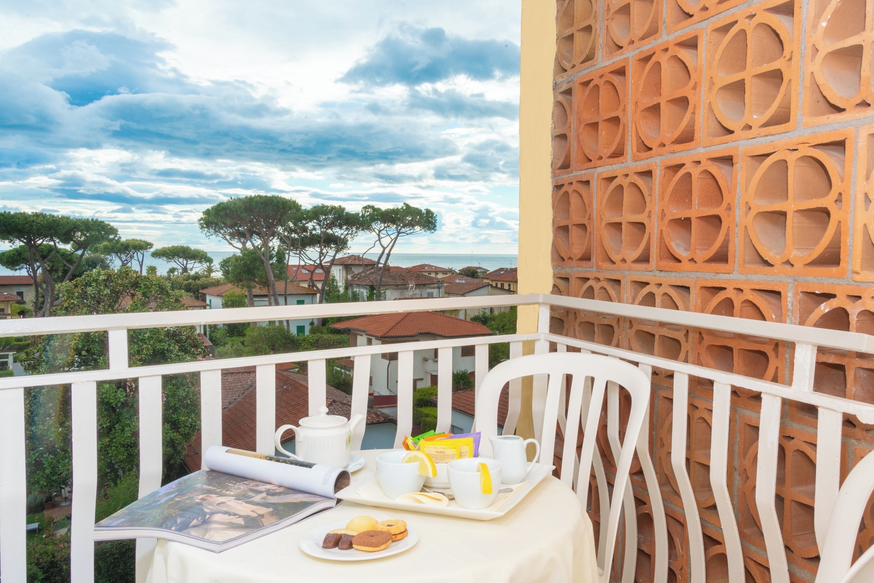 Un balcón con una mesa lista para el desayuno, una silla blanca y un muro decorativo.