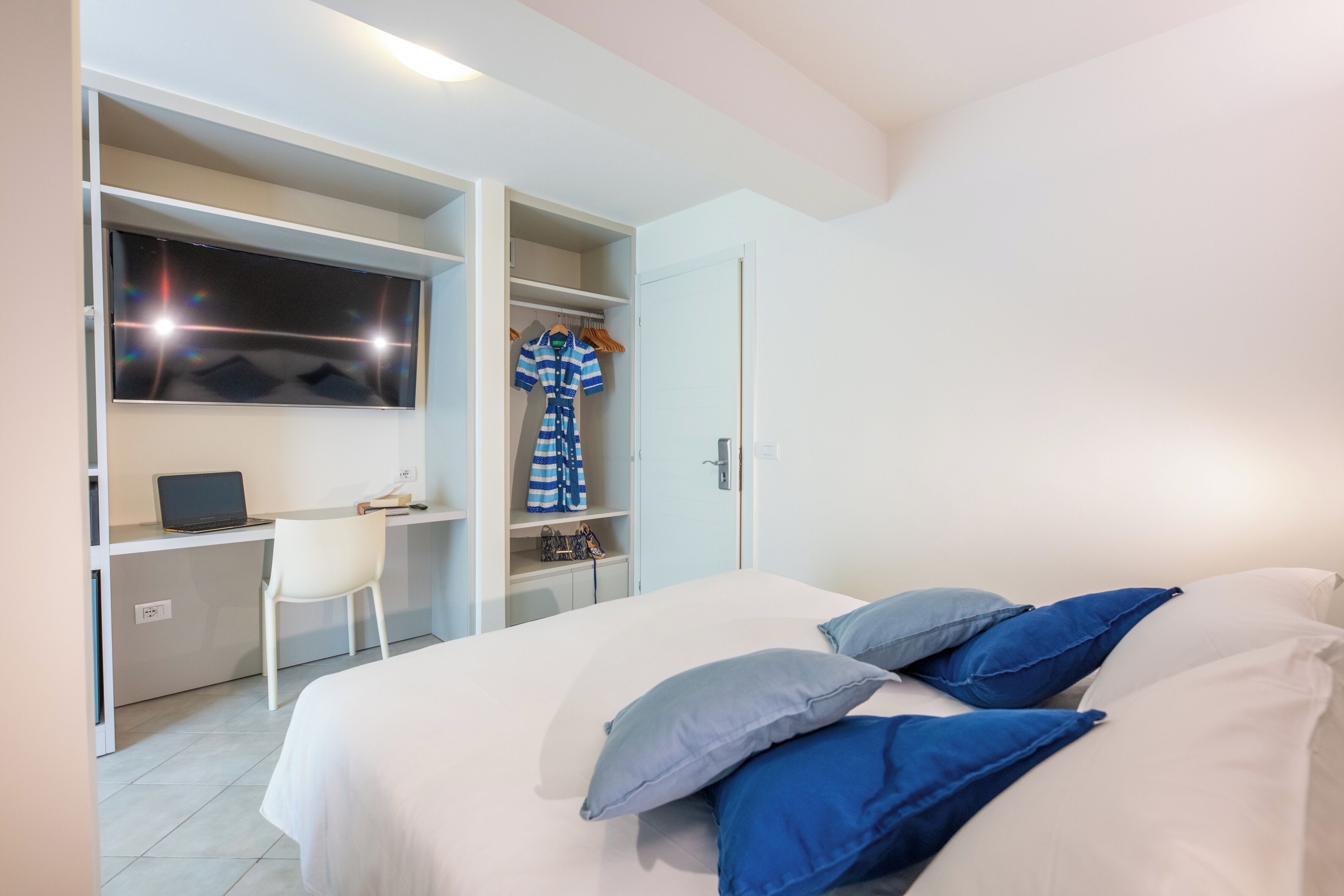 Une chambre à coucher avec un lit, des oreillers, un bureau avec un ordinateur portable et une armoire.