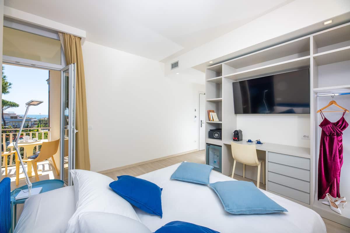 A hotel room with a bed, a desk, a TV, and a balcony with a table and chairs.