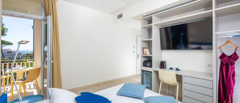 A hotel room with a bed, a desk, a TV, and a balcony with a table and chairs.
