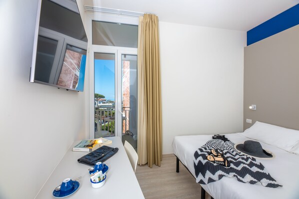 Una habitación de hotel con una cama, un escritorio con un teclado, una taza y un libro.
