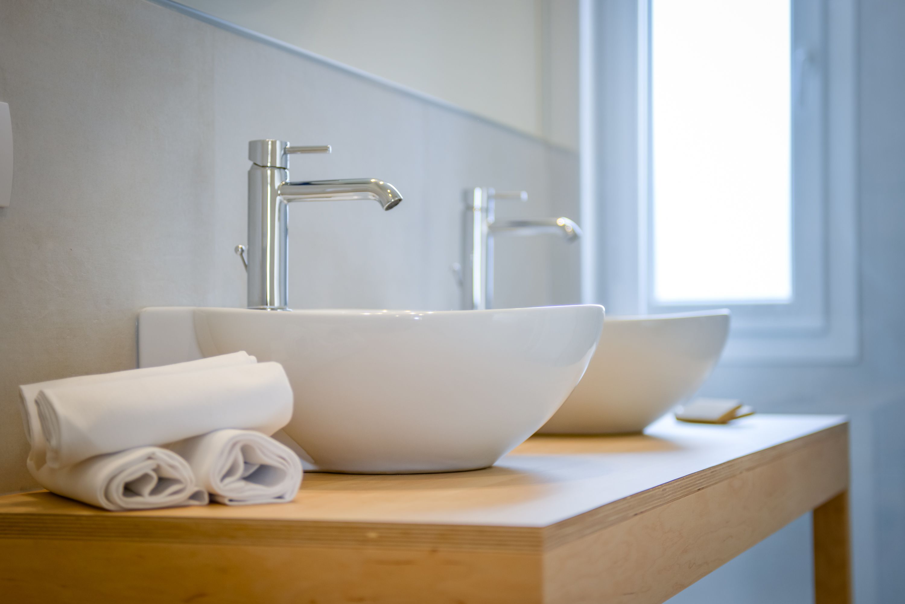 Un baño con un lavabo grande blanco, un grifo moderno y toallas dobladas impecablemente sobre una encimera de madera.