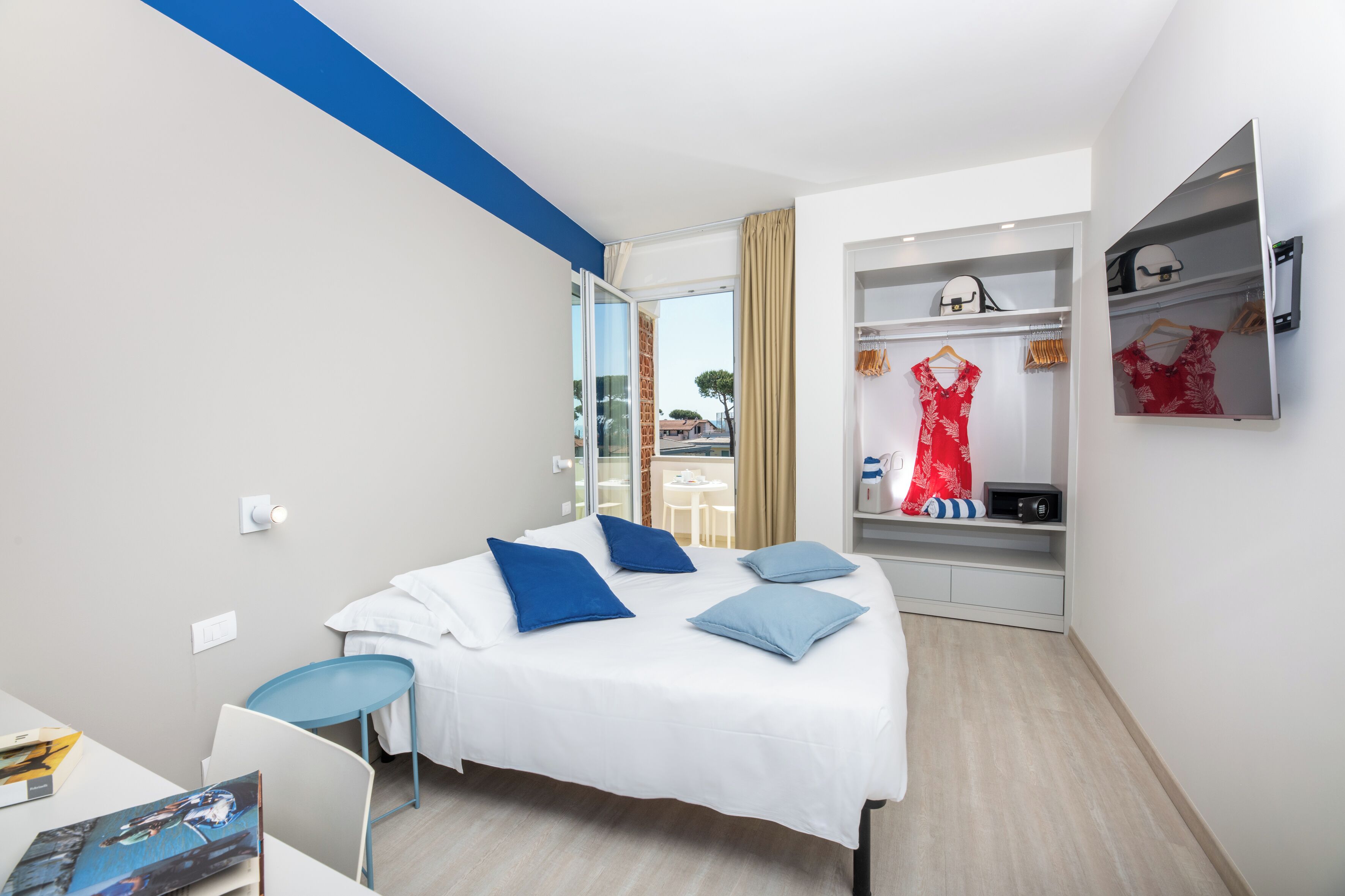 A modern hotel room with a bed, a desk, and a wardrobe.