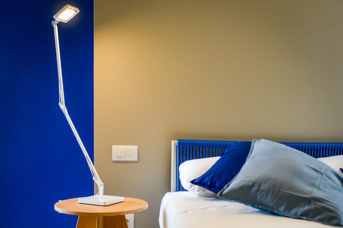 A bedroom with a bed, a bedside table with a lamp, and a wall switch.