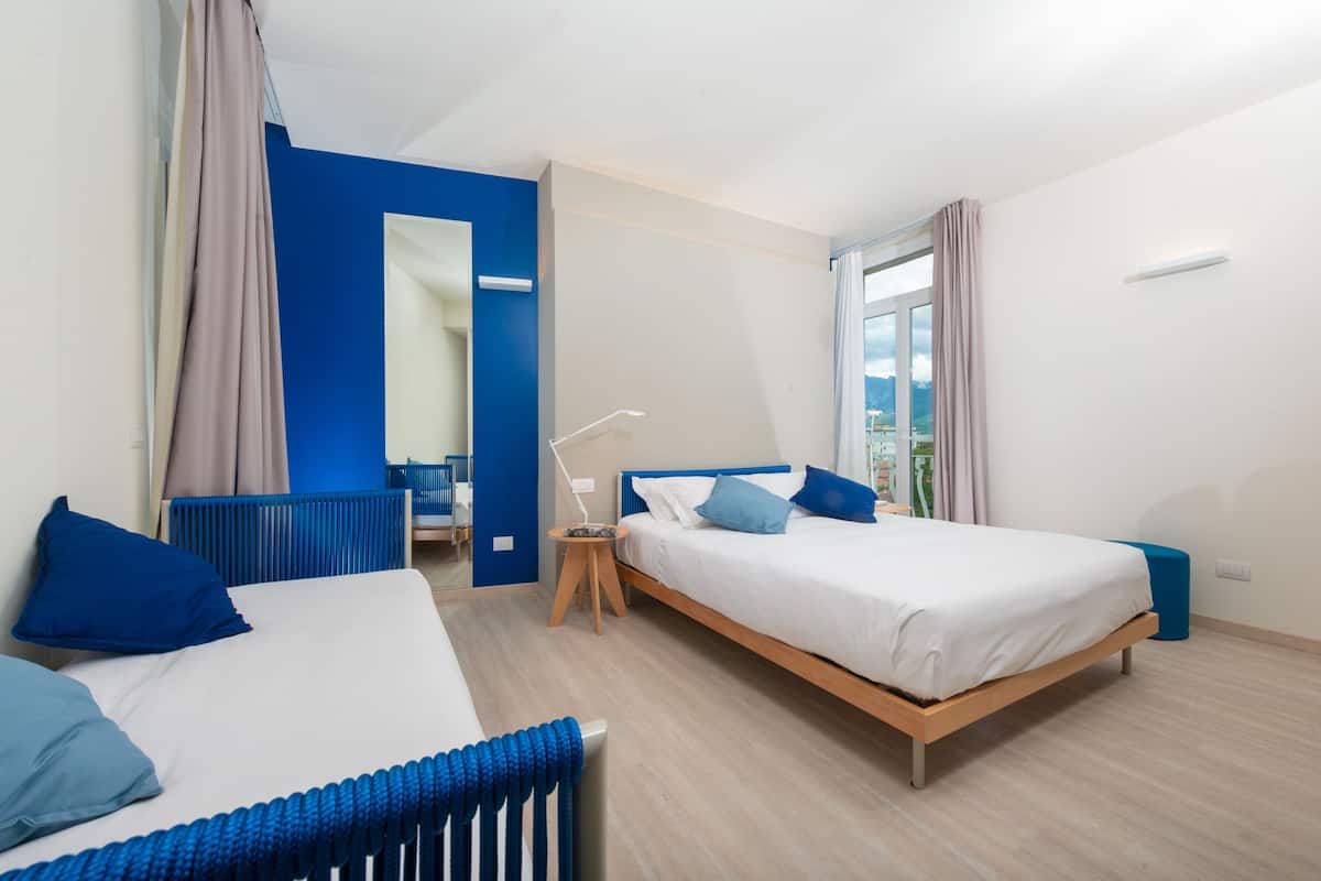 A modern bedroom with a large bed, a smaller bed, a desk, and a mirror.