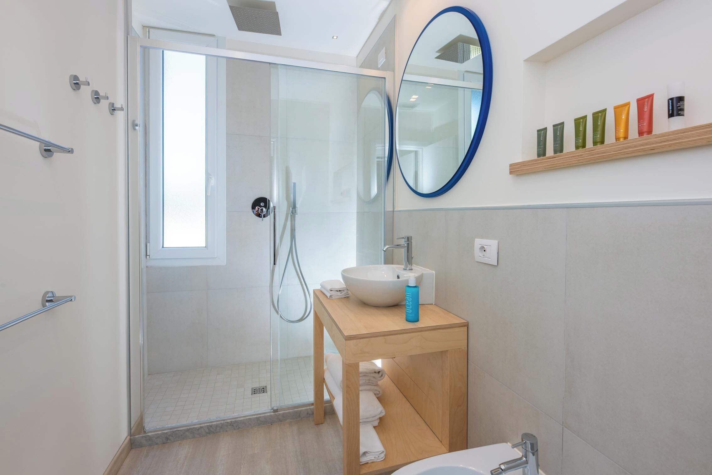 Ein modernes Badezimmer mit einer Glaskabine zur Dusche, einem hölzernen Waschtisch mit Waschbecken und einem Spiegel darüber.