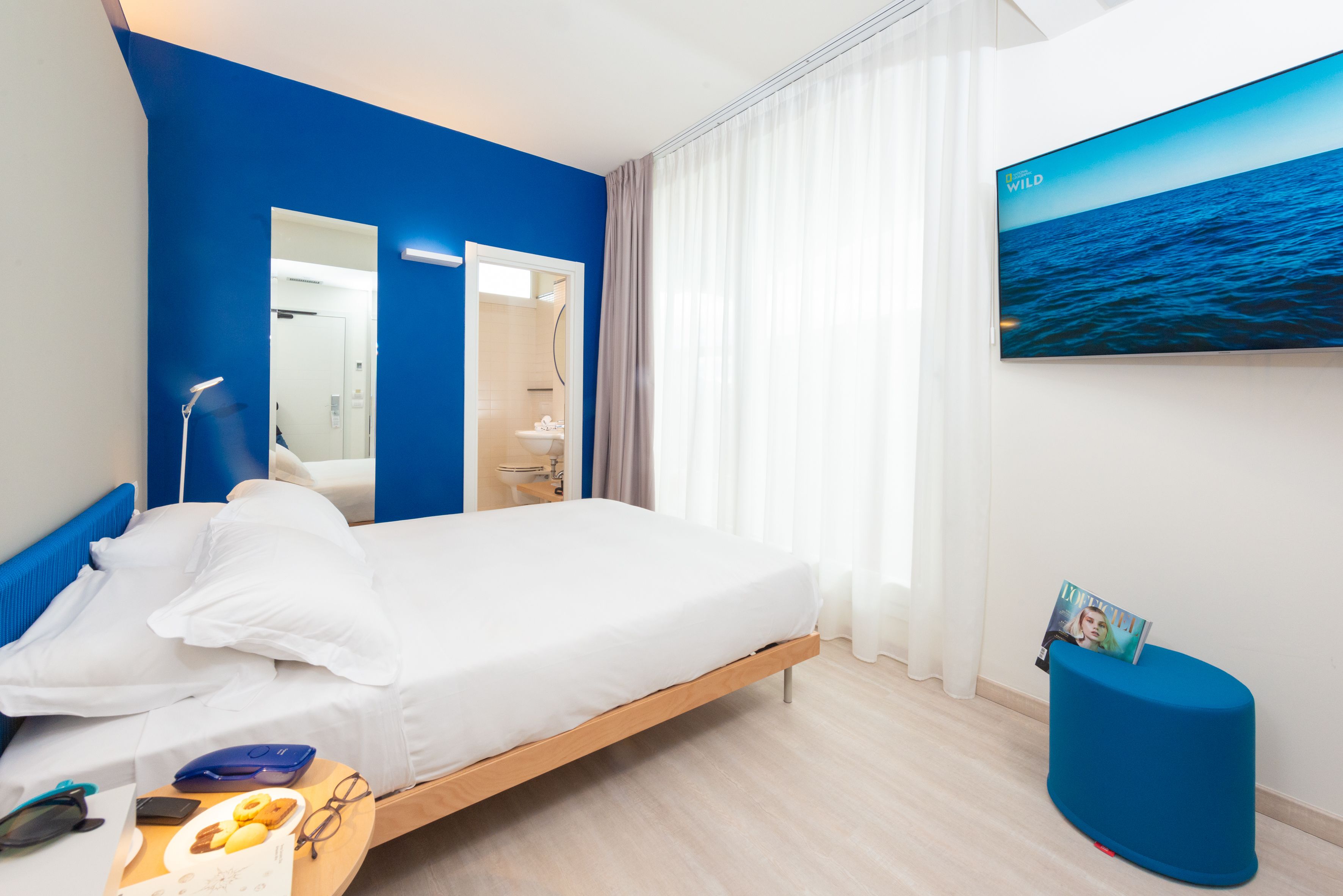 Una habitación de hotel moderna con cama, espejo, televisión y vista al océano.