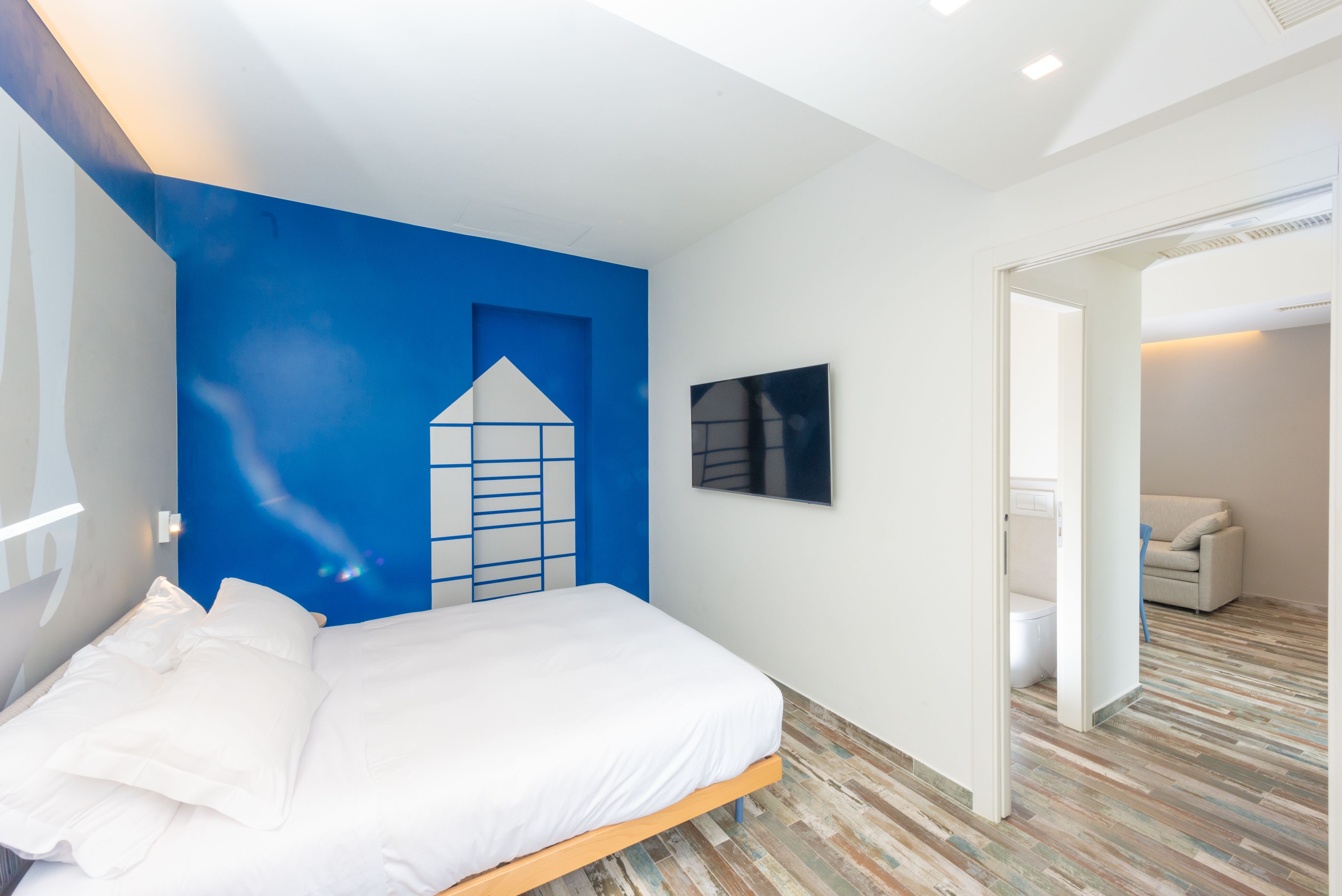 Une chambre à coucher avec un lit, un mur d’accent bleu, un tableau encadré et un plancher en bois.