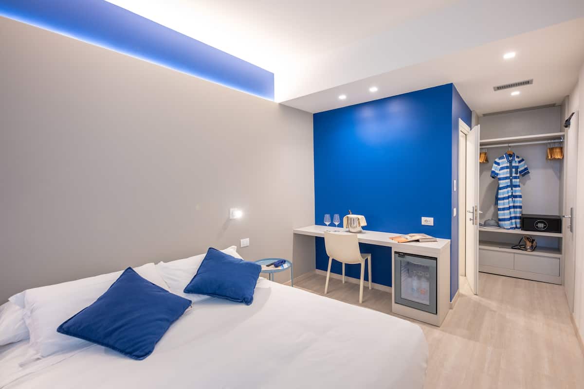 A modern hotel room with a bed, desk, and walk-in closet.