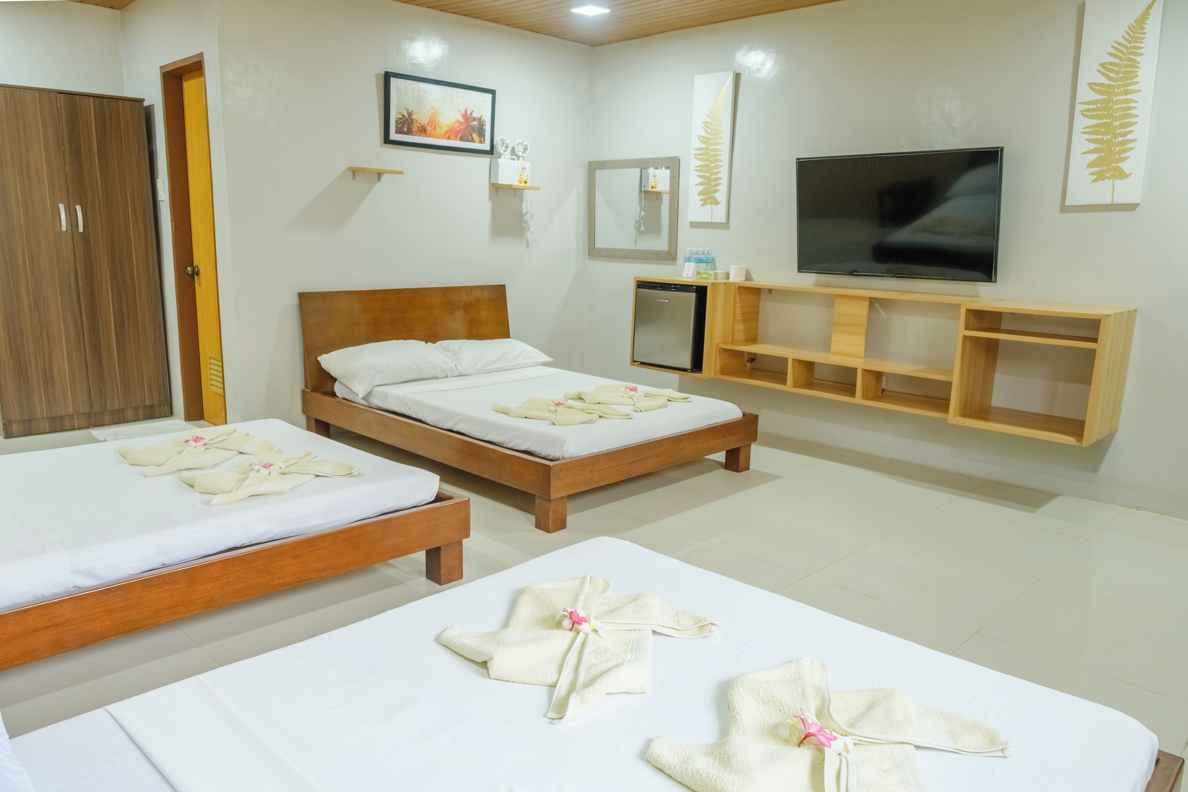 A hotel room with two wooden beds, a TV, a small fridge, and a wooden cabinet.