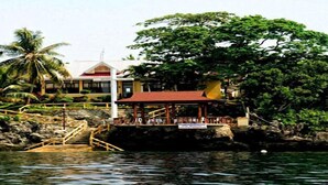 A coastal hotel with a red-roofed building, a wooden staircase leading to a dock, and lush tropical vegetation. - Panglao Kalikasan Dive Resort (Panglao)