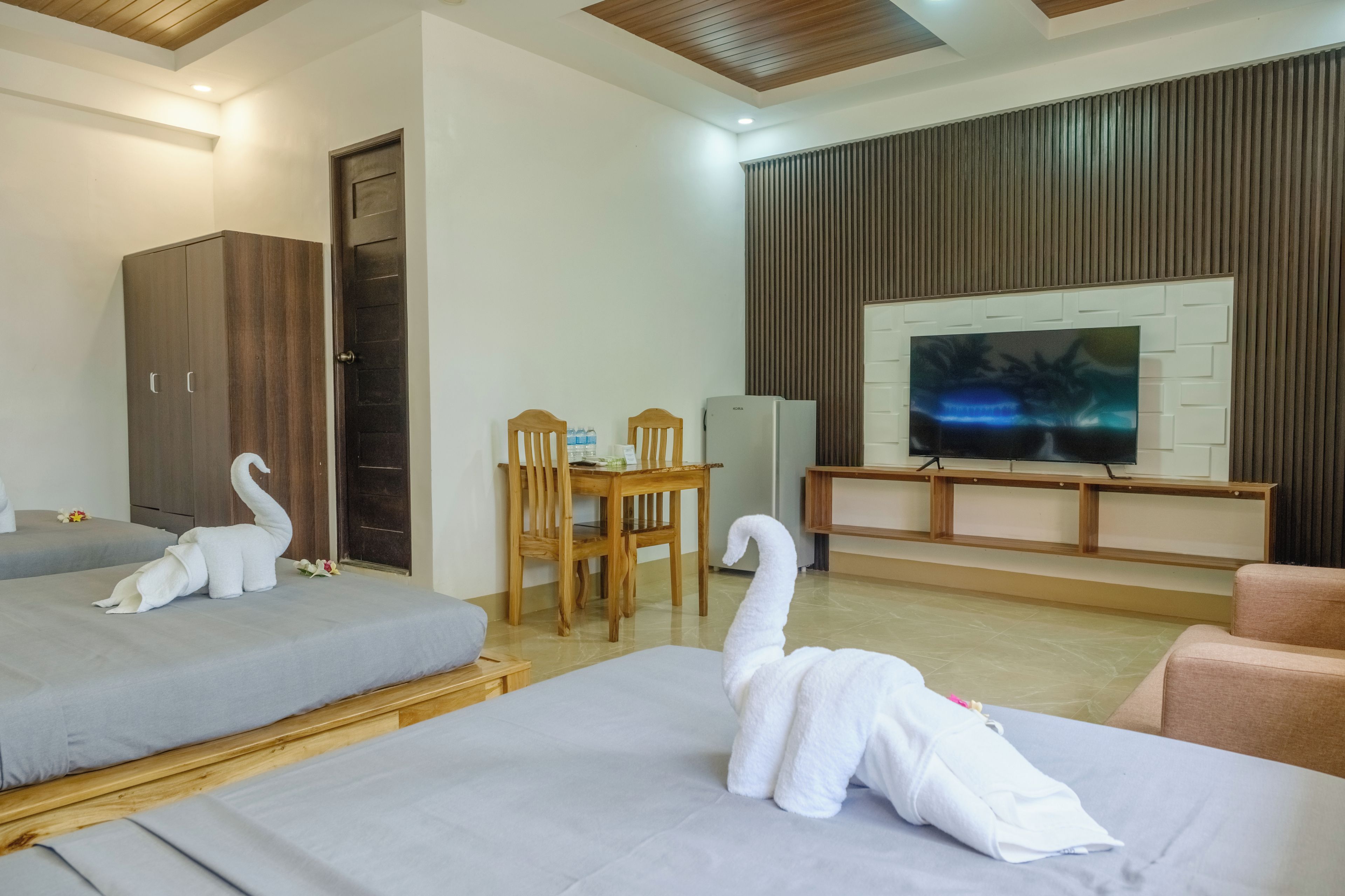 Habitación de hotel con dos camas, un armario de madera, un televisor y una mesa de comedor con sillas.