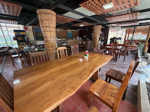 Een ruime eethoek met een grote houten tafel, meerdere houten stoelen en een hoog plafond met een uniek geweven patroon.