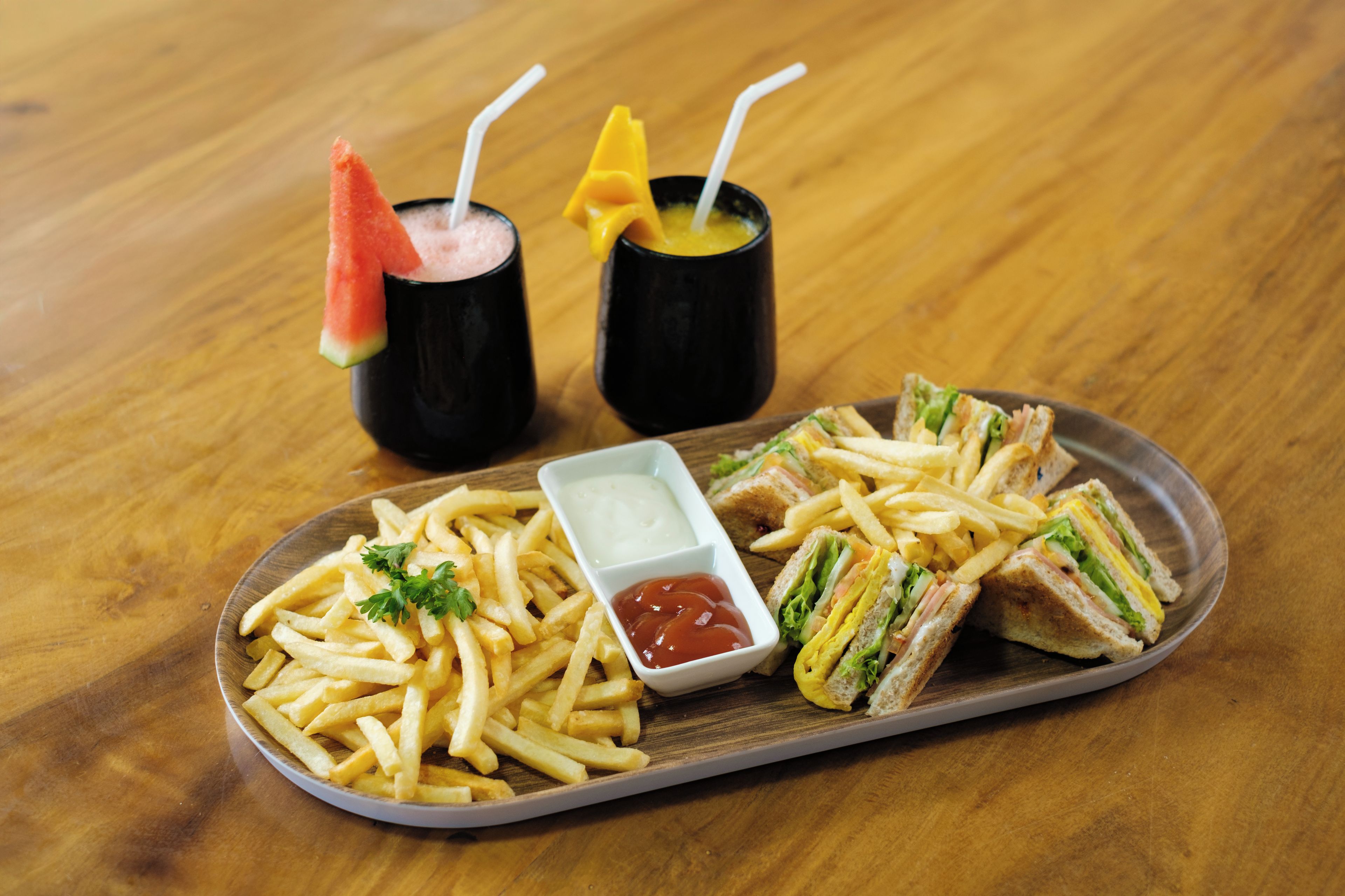 A tray with French fries, a sandwich cut in half, and two drinks with straws.