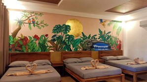 A hotel room with three wooden beds, each with a grey mattress and pillows. The room features a large mural on the wall depicting tropical foliage and a waterfall. - Panglao Kalikasan Dive Resort (Panglao)
