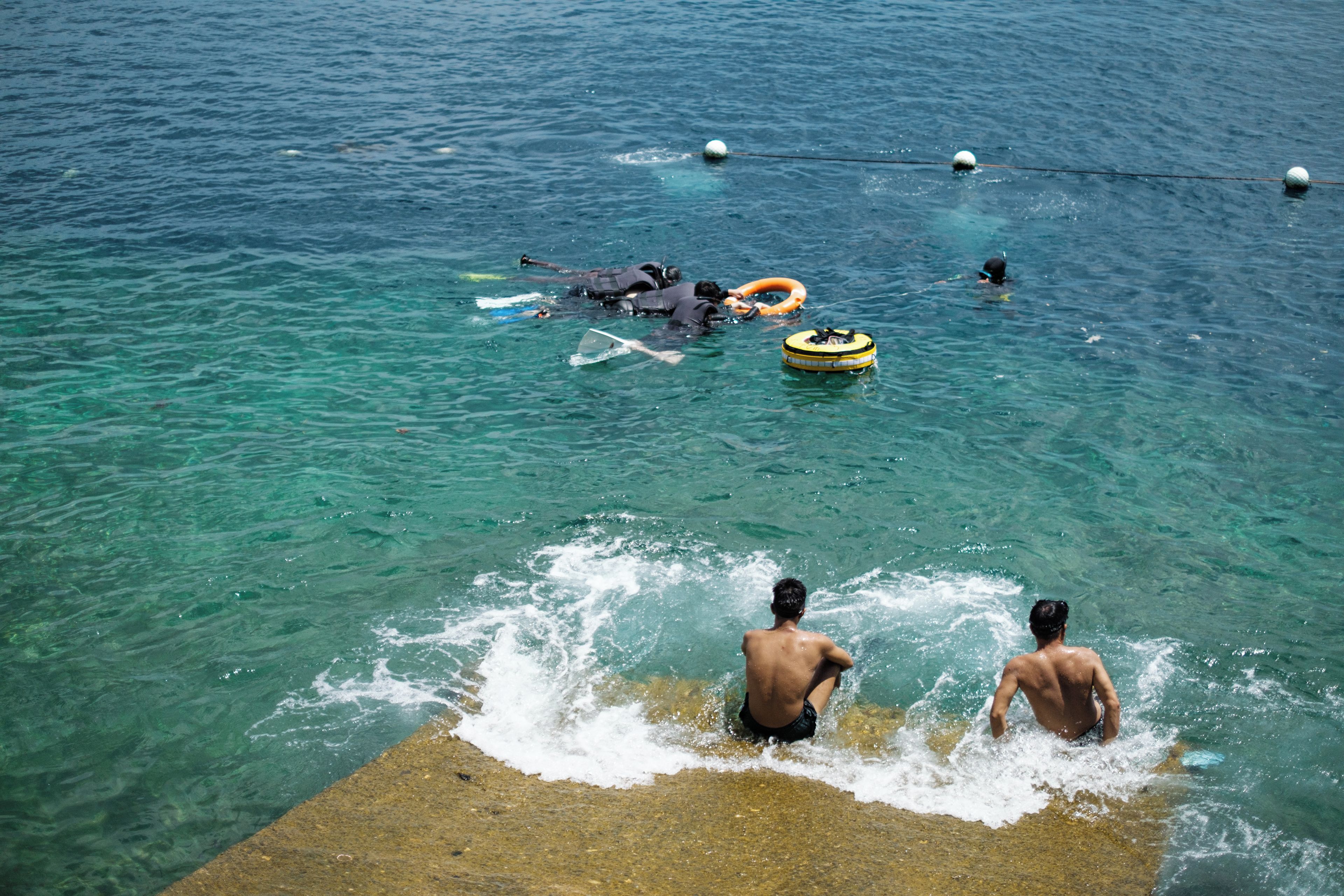A beach scene with clear water, people swimming, and floating devices.