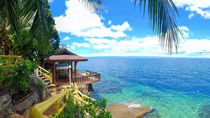 A wooden gazebo with a balcony overlooking a clear blue sea, surrounded by lush greenery and a rocky shoreline. - Panglao Kalikasan Dive Resort (Panglao)
