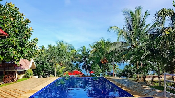 A swimming pool with a tiled edge, surrounded by palm trees and a clear blue sky. - Panglao Kalikasan Dive Resort (Panglao)