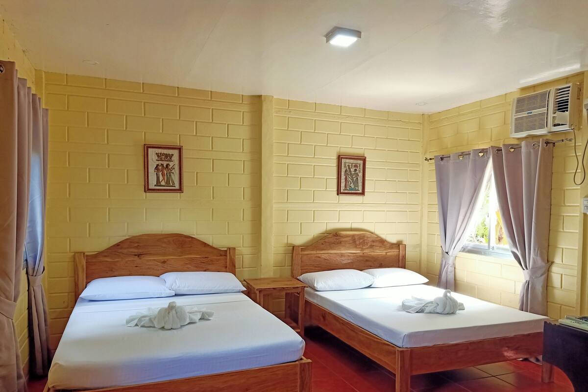 A room with two wooden beds, a brick wall, and a window with curtains.