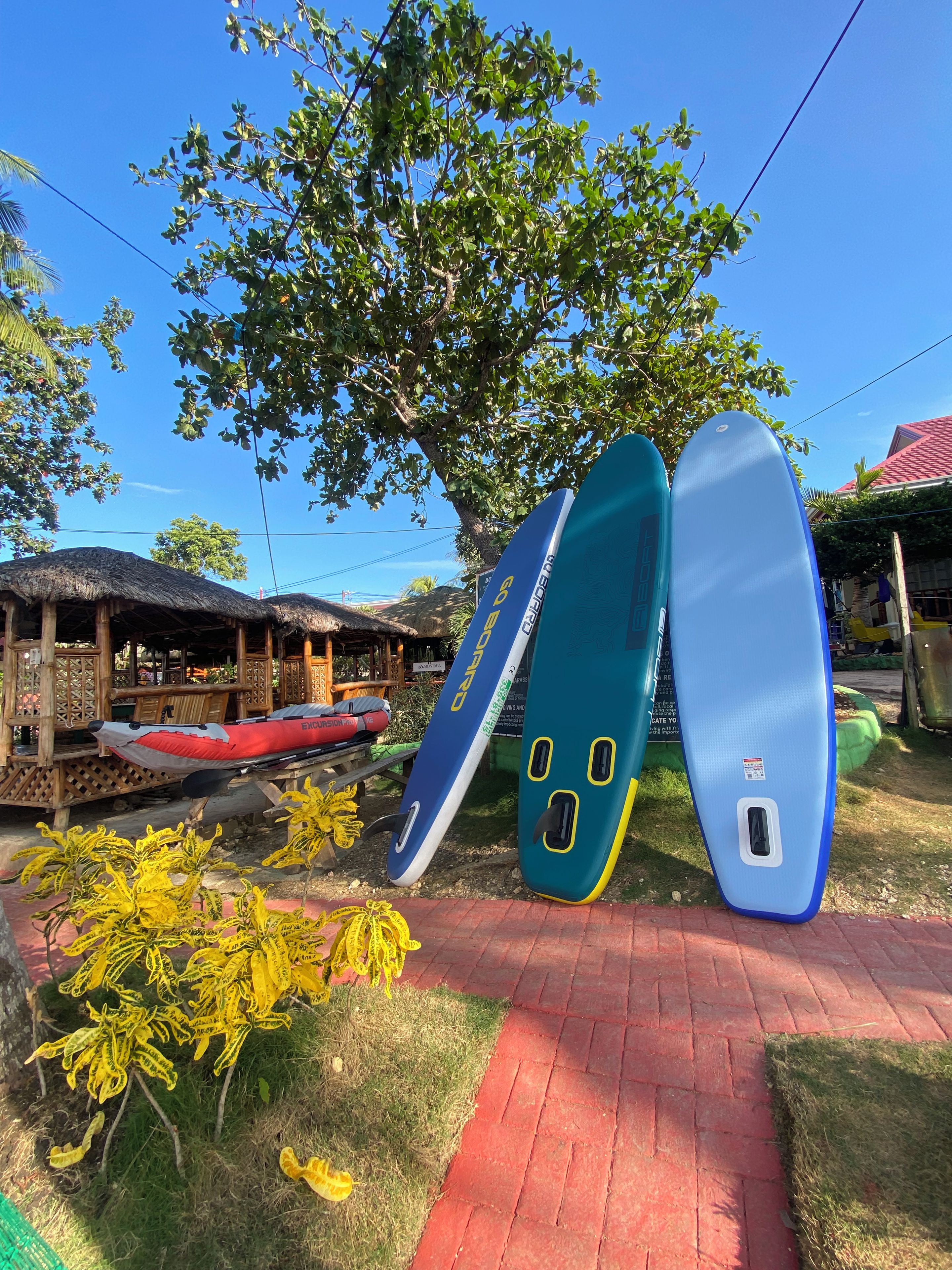 Una estructura de madera con techo de paja, una tabla de surf apoyada y un cielo azul despejado.