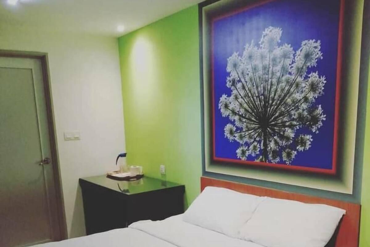 Una habitación de hotel con una cama, una mesita de noche, un cuadro con un árbol y una puerta.
